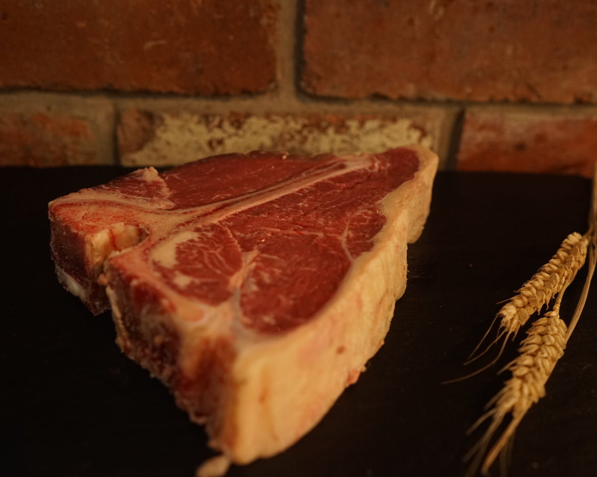 A fresh Aberdeen Angus T-bone steak on a dark surface with a brick wall in the background.